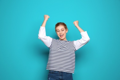 Happy young woman celebrating victory on color background