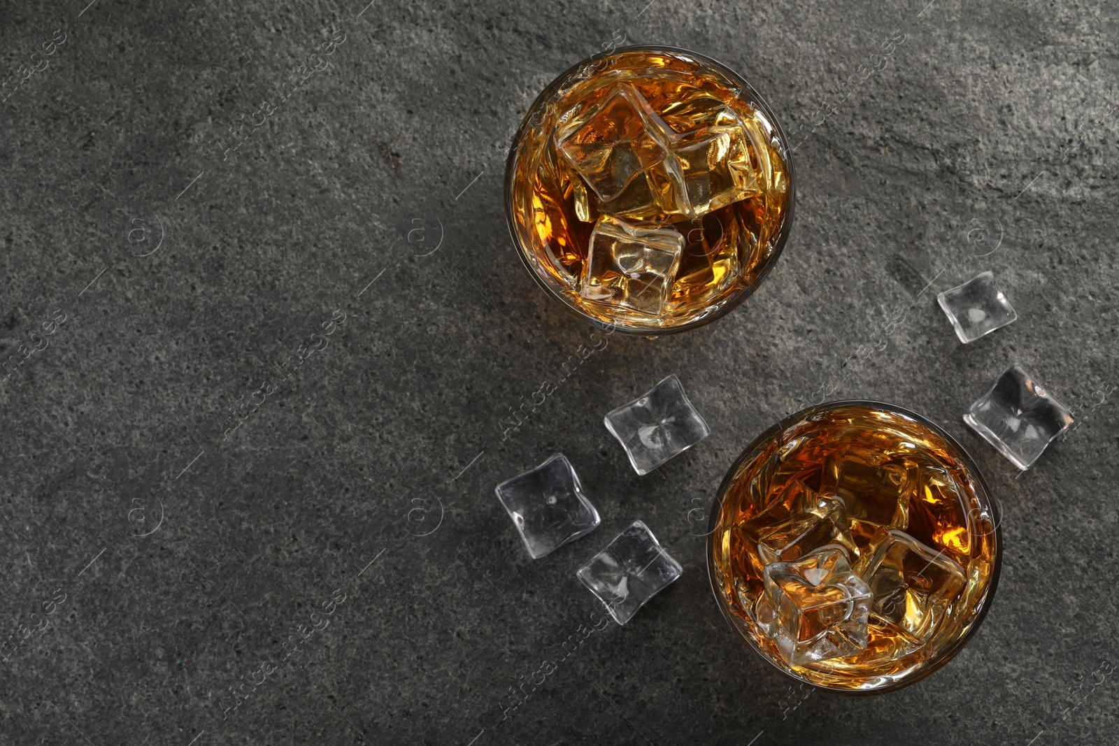 Photo of Whiskey and ice cubes in glasses on grey textured table, top view. Space for text