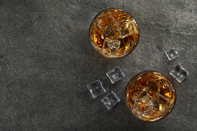 Whiskey and ice cubes in glasses on grey textured table, top view. Space for text