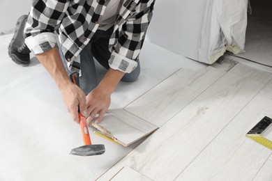 Photo of Professional worker using hammer during installation of new laminate flooring indoors, closeup