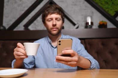 Photo of Handsome man with cup of coffee using smartphone at table in cafe, focus on hands