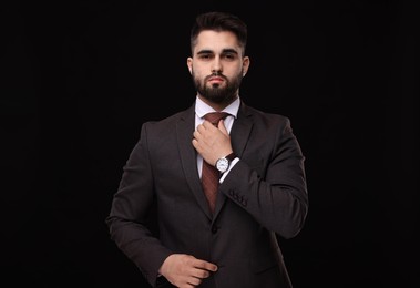 Handsome businessman in suit and necktie on black background