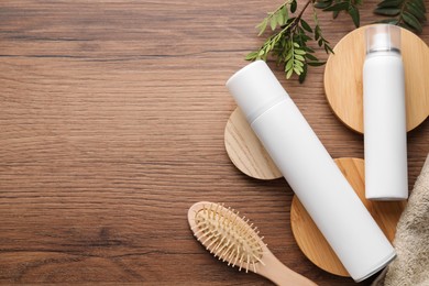 Photo of Dry shampoo sprays, green leaves and hairbrush on wooden table, flat lay. Space for text