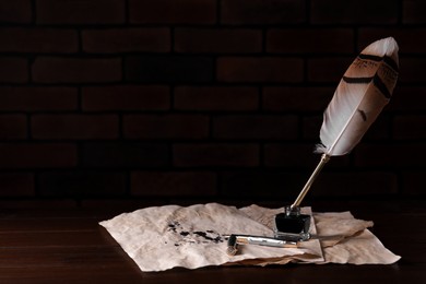 Photo of Inkwell with feather pen and vintage parchment with ink stains on wooden table against black background. Space for text