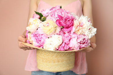 Woman with bouquet of beautiful peonies in hat on beige background, closeup