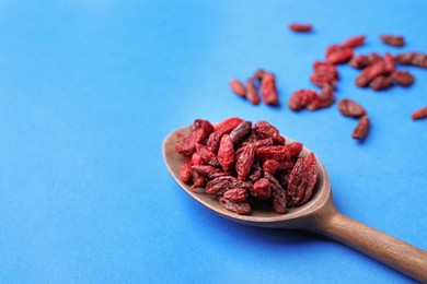 Dried goji berries in spoon on blue background, closeup. Space for text