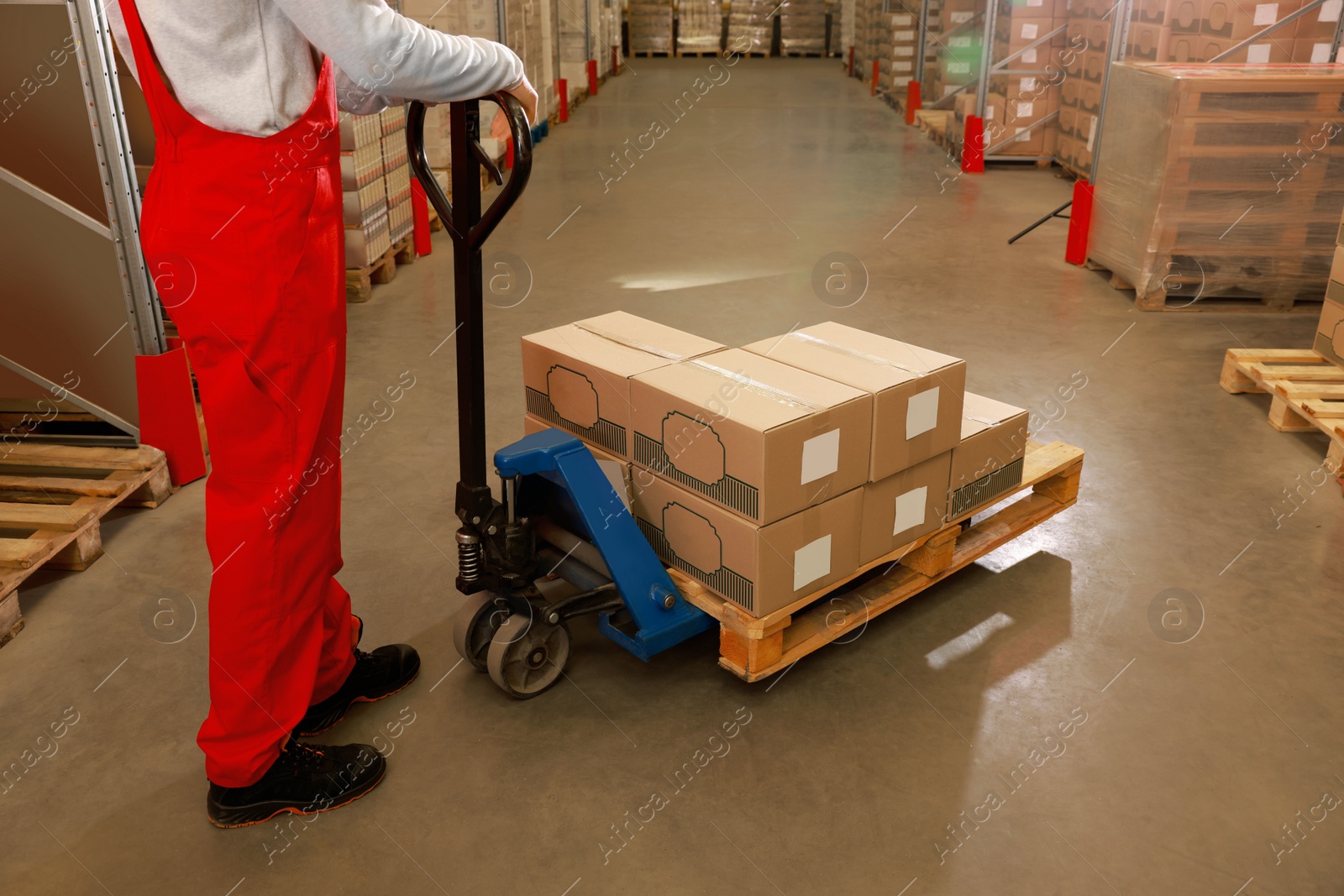 Image of Worker moving cardboard boxes with manual forklift in warehouse, closeup. Logistics concept