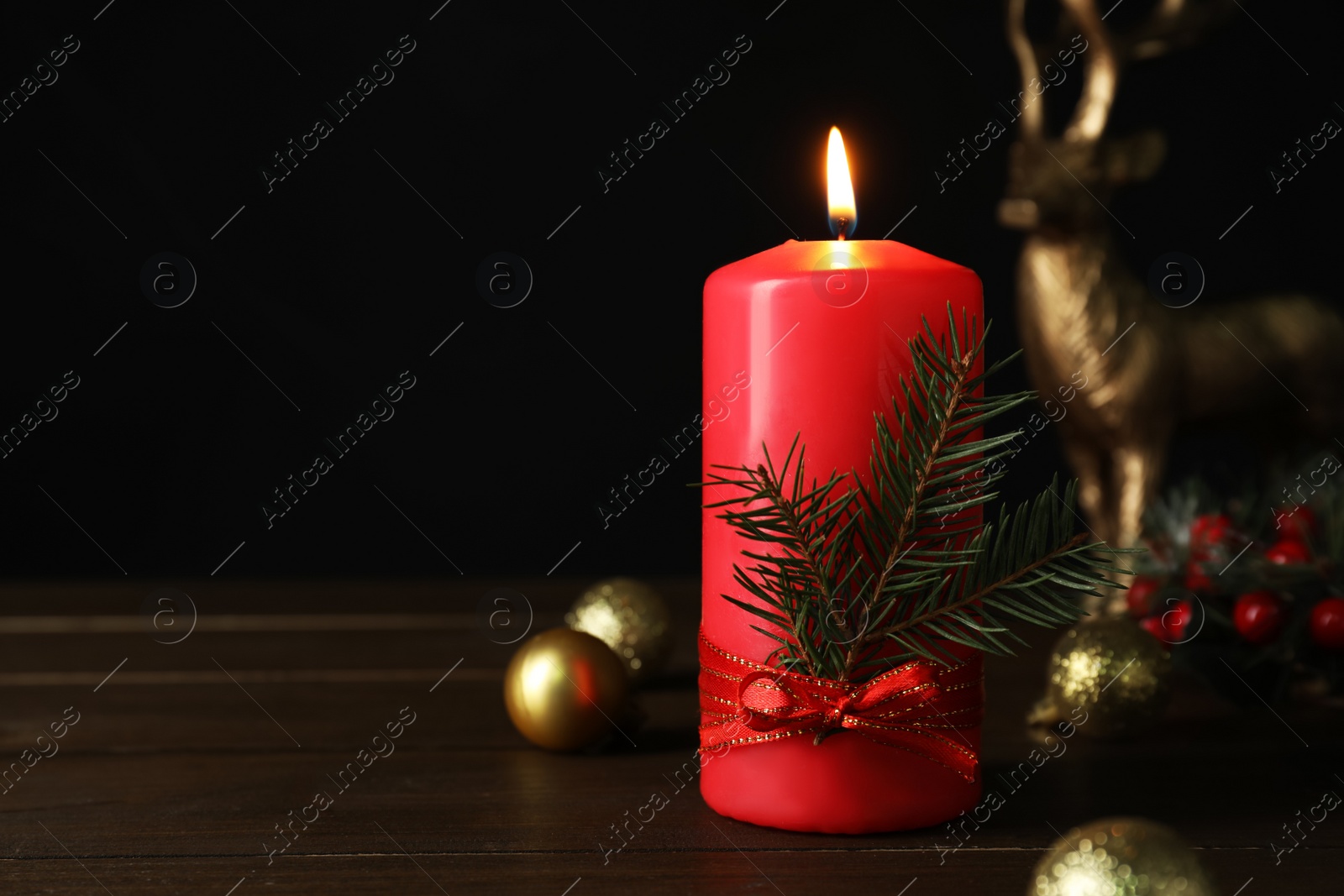 Photo of Red burning candle and Christmas decor on wooden table against black background. Space for text