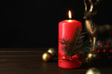 Photo of Red burning candle and Christmas decor on wooden table against black background. Space for text