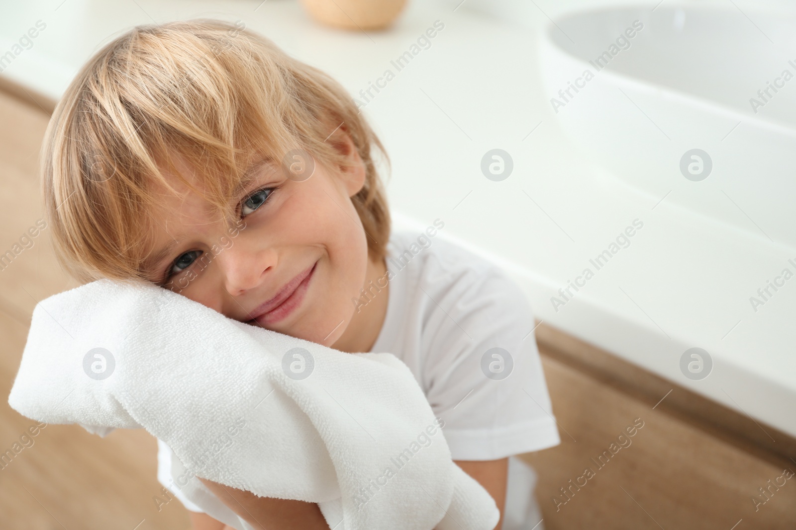 Photo of Cute little boy wiping face with towel in bathroom