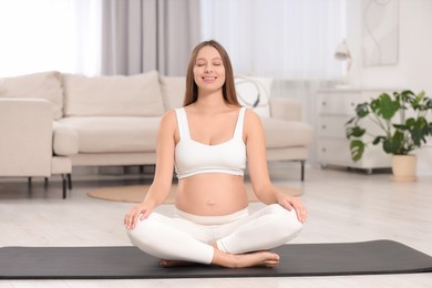 Photo of Pregnant woman meditating on yoga mat at home