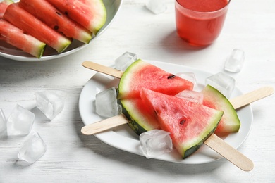 Plate with watermelon popsicles and ice cubes on table