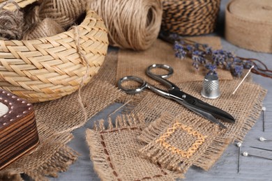 Pieces of burlap fabric with different stitches and sewing tools on grey table