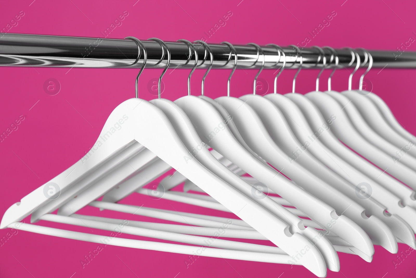 Photo of Metal rack with clothes hangers on color background, closeup