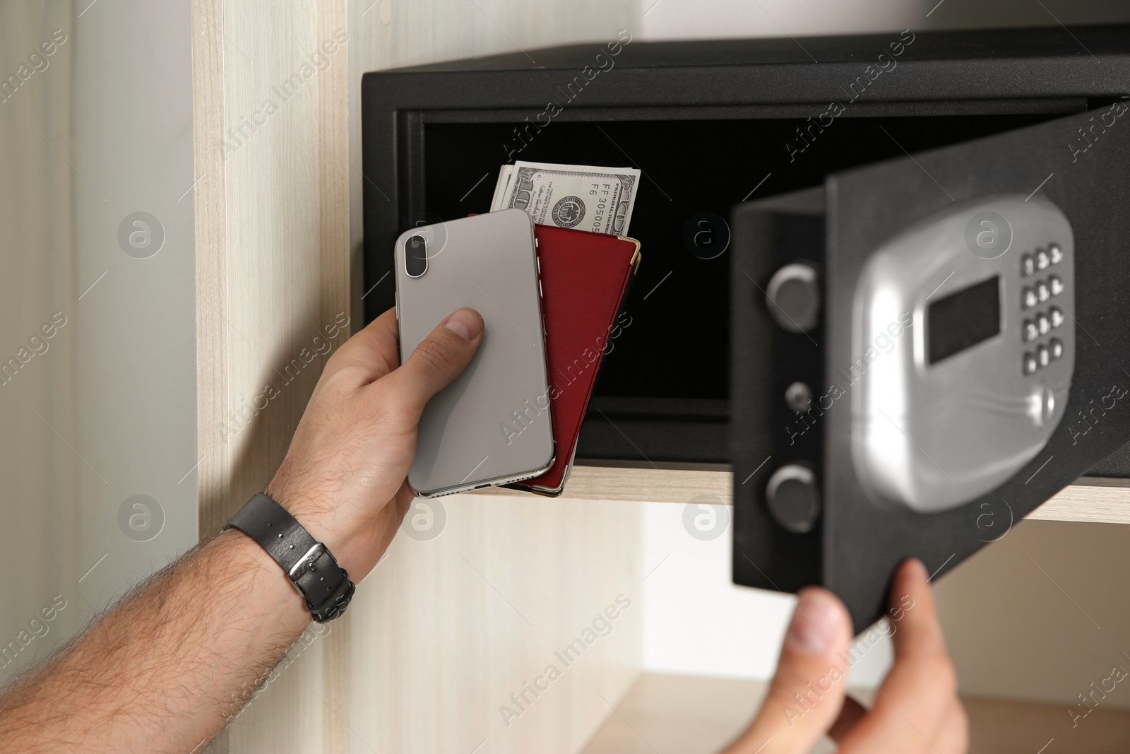 Photo of Man putting smartphone, passport and money into steel safe, closeup