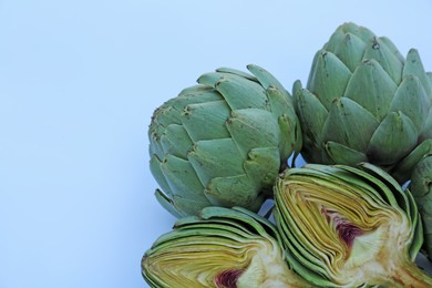 Photo of Cut and whole fresh raw artichokes on light blue background, flat lay. Space for text