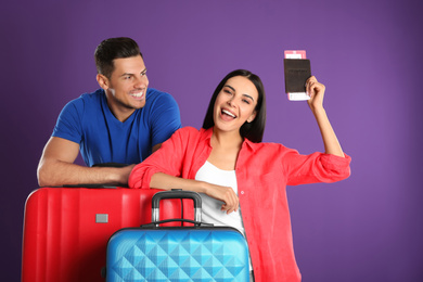 Happy couple with suitcases for summer trip on purple background. Vacation travel