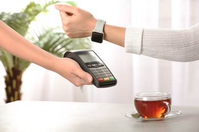 Woman using terminal for contactless payment with smart watch at table, closeup