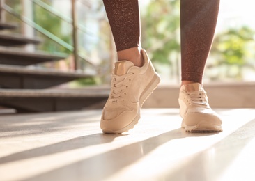 Young woman wearing stylish sneakers indoors, closeup