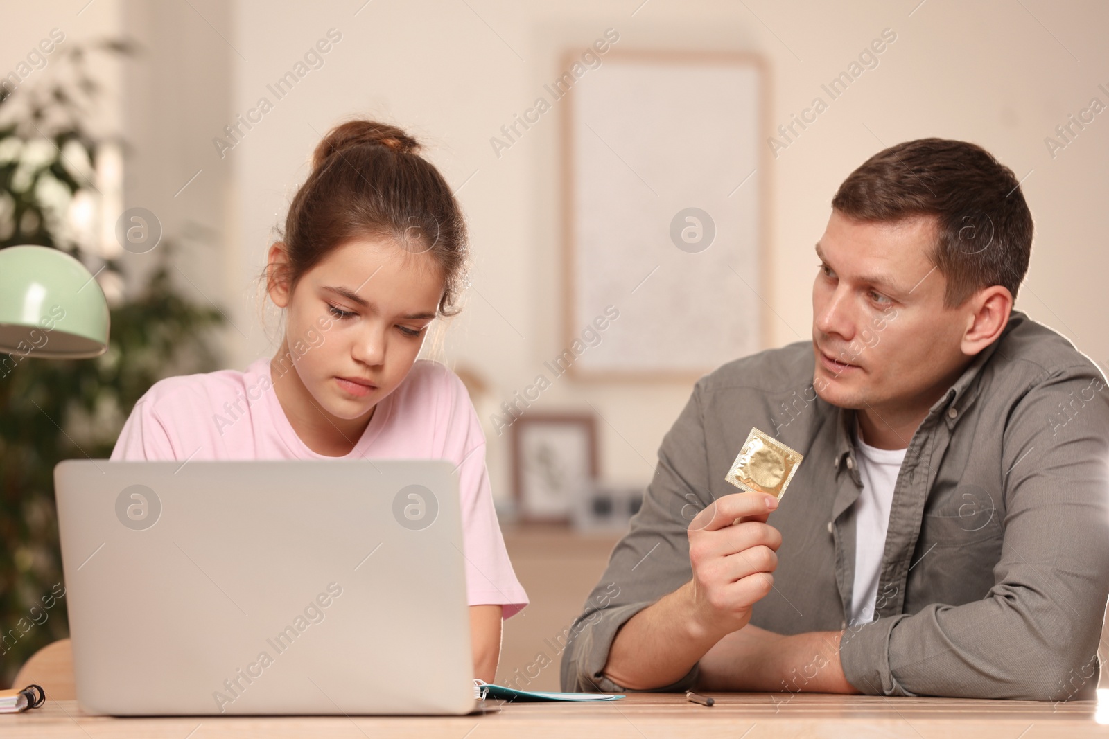 Photo of Father talking with his teenage daughter about contraception while she using laptop at home. Sex education concept