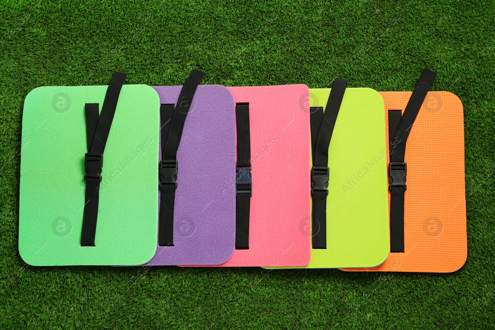 Photo of Bright foam tourist seat mats on green grass, flat lay