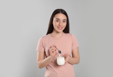 Portrait of happy woman with tasty yogurt on grey background