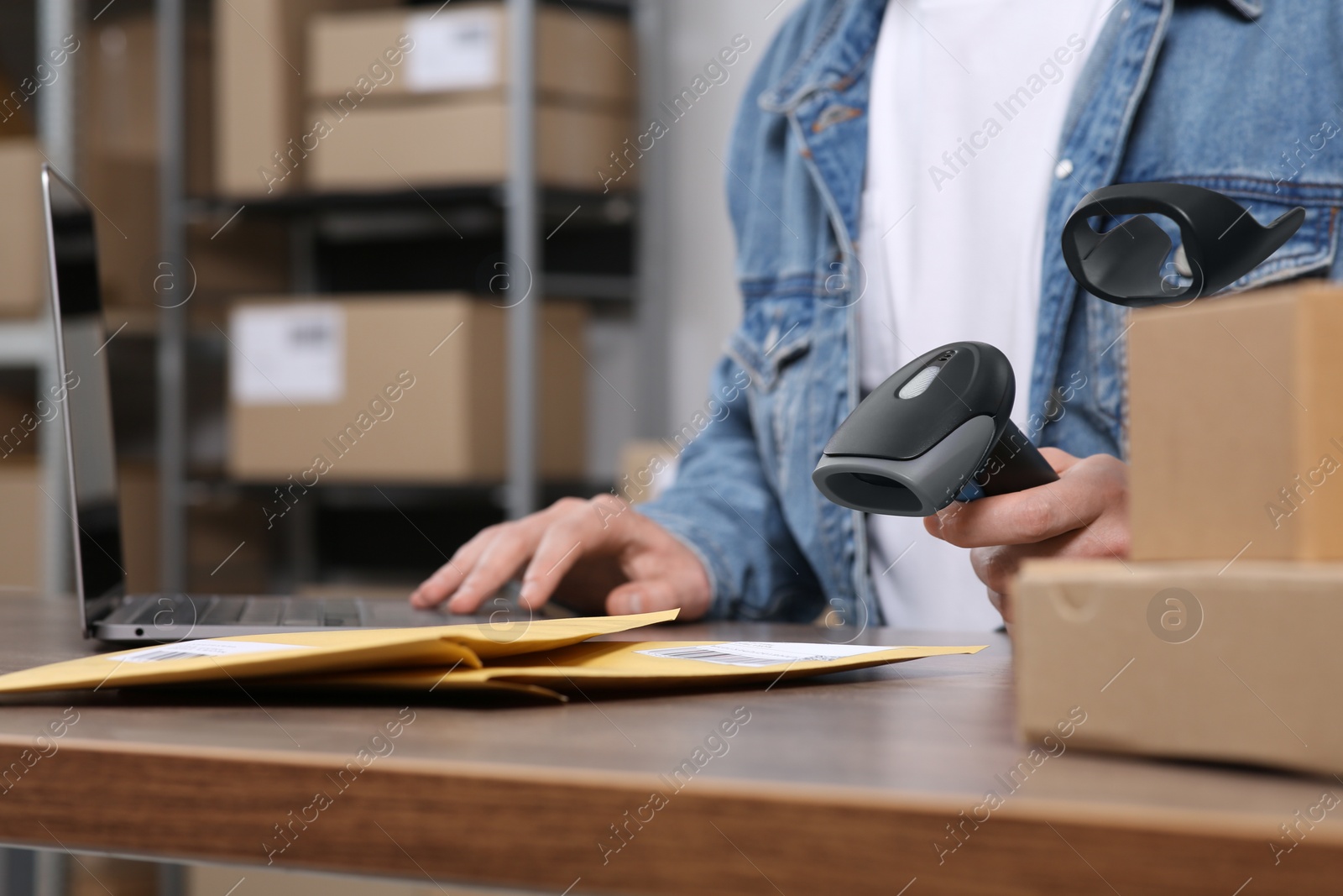 Photo of Seller with scanner, parcels and laptop at table in office, closeup. Online store