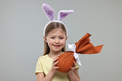 Photo of Easter celebration. Cute girl with bunny ears holding wrapped gift on gray background