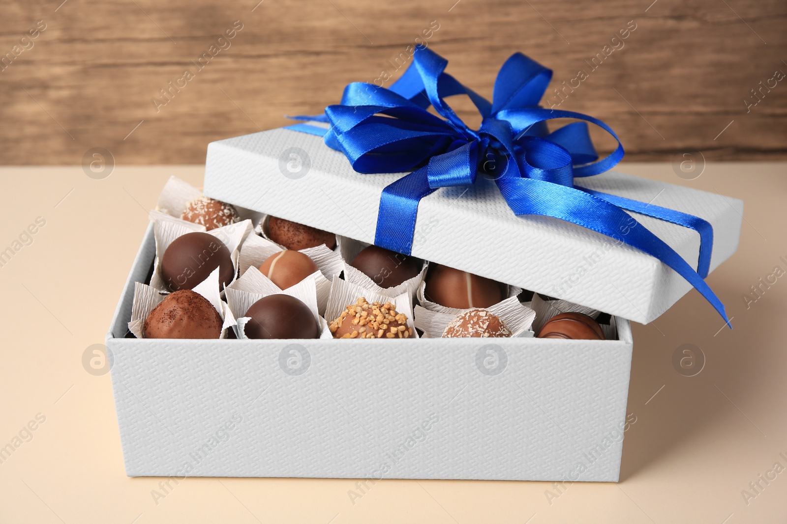 Photo of Box with delicious chocolate candies on beige background, closeup