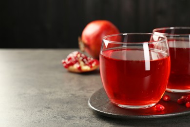 Photo of Tasty pomegranate juice in glasses and fresh fruits on grey table, closeup. Space for text