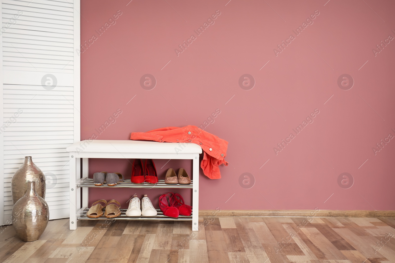 Photo of Collection of stylish shoes on rack storage near color wall in room