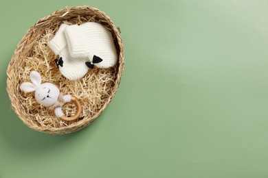 Different baby accessories in wicker box on green background, top view. Space for text