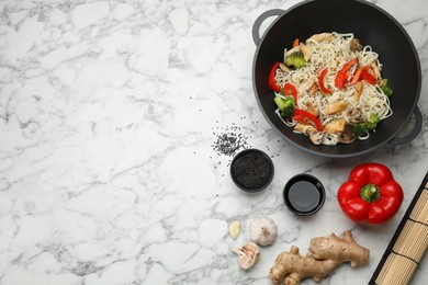 Stir fried noodles with chicken and vegetables in wok on white marble table, flat lay. Space for text