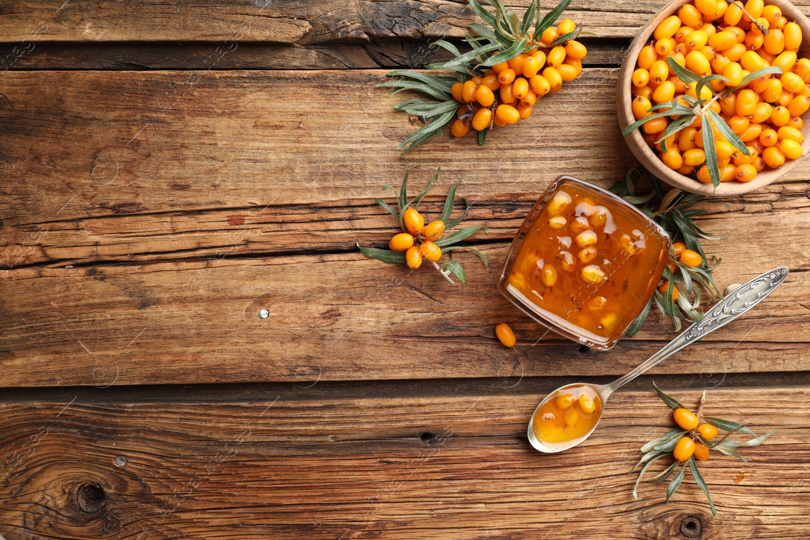 Photo of Delicious sea buckthorn jam and fresh berries on wooden table, flat lay. Space for text