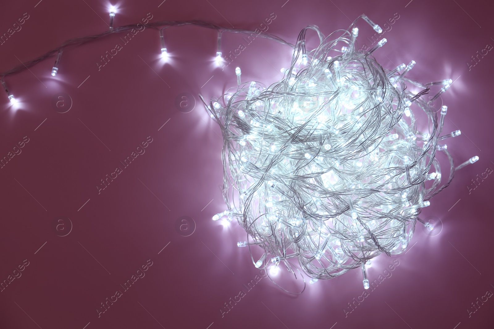 Photo of Glowing Christmas lights on violet background, top view. Space for text