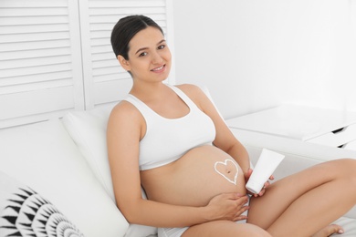 Photo of Beautiful pregnant woman with body cream sitting on sofa at home