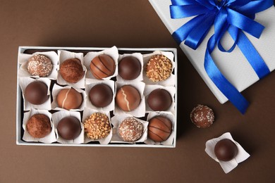 Photo of Box with delicious chocolate candies on brown background, flat lay
