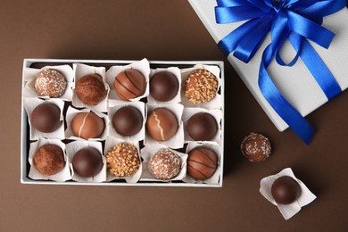 Box with delicious chocolate candies on brown background, flat lay