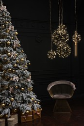 Beautiful decorated Christmas tree, chair and festive decor in dark room. Interior design