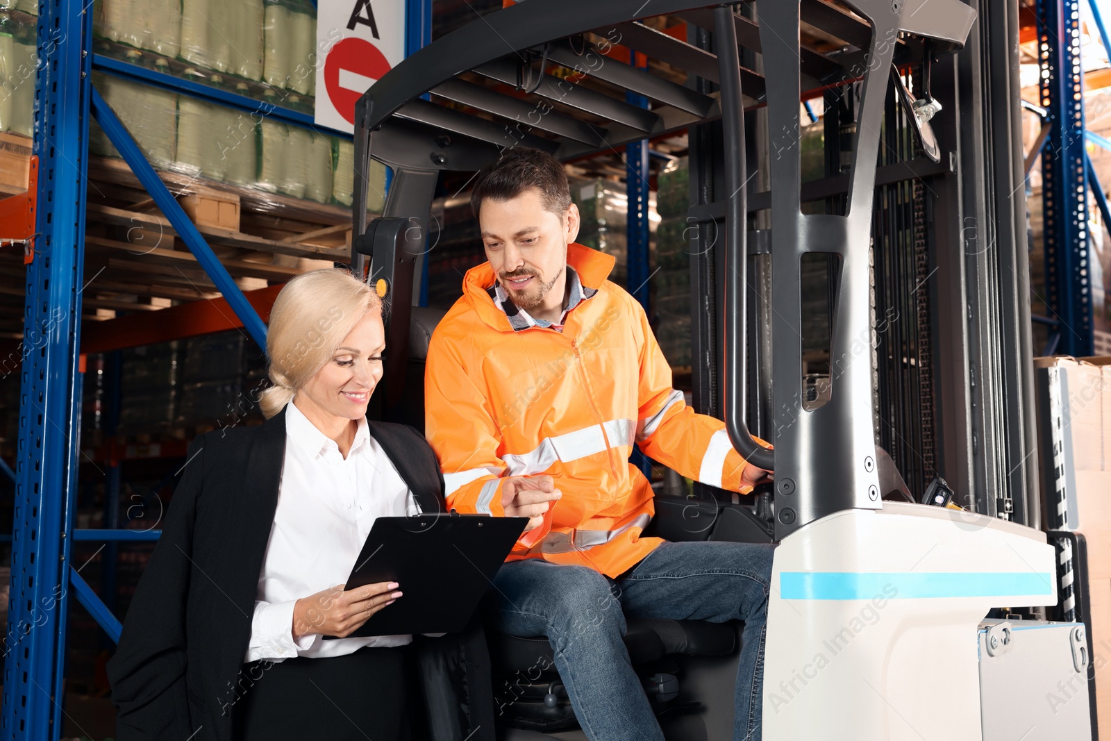 Photo of Worker talking with manager while sitting in forklift truck at warehouse