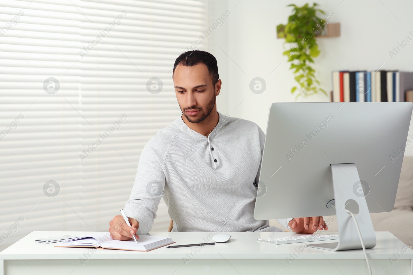 Photo of Young man working on computer at desk in room. Home office