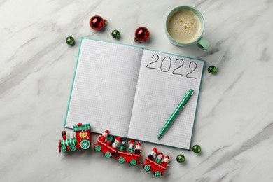Photo of Open planner, cup of coffee and Christmas decor on white marble background, flat lay. 2022 New Year aims
