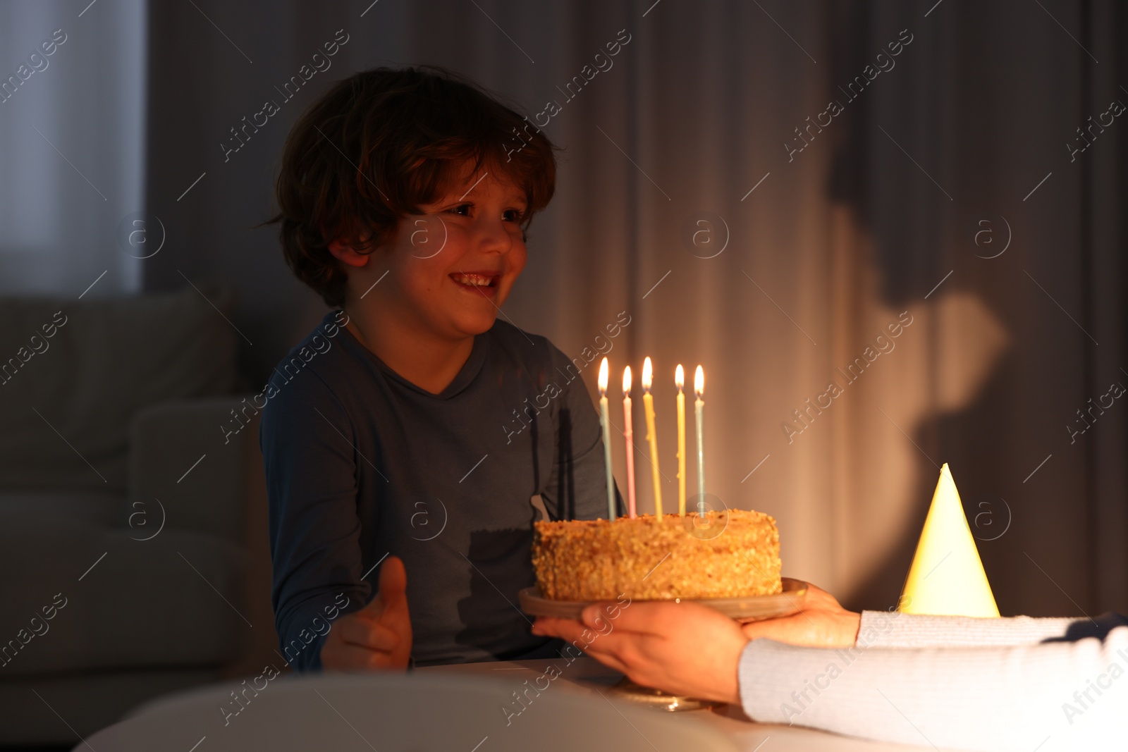 Photo of Birthday celebration. Mother holding tasty cake with burning candles near her son indoors