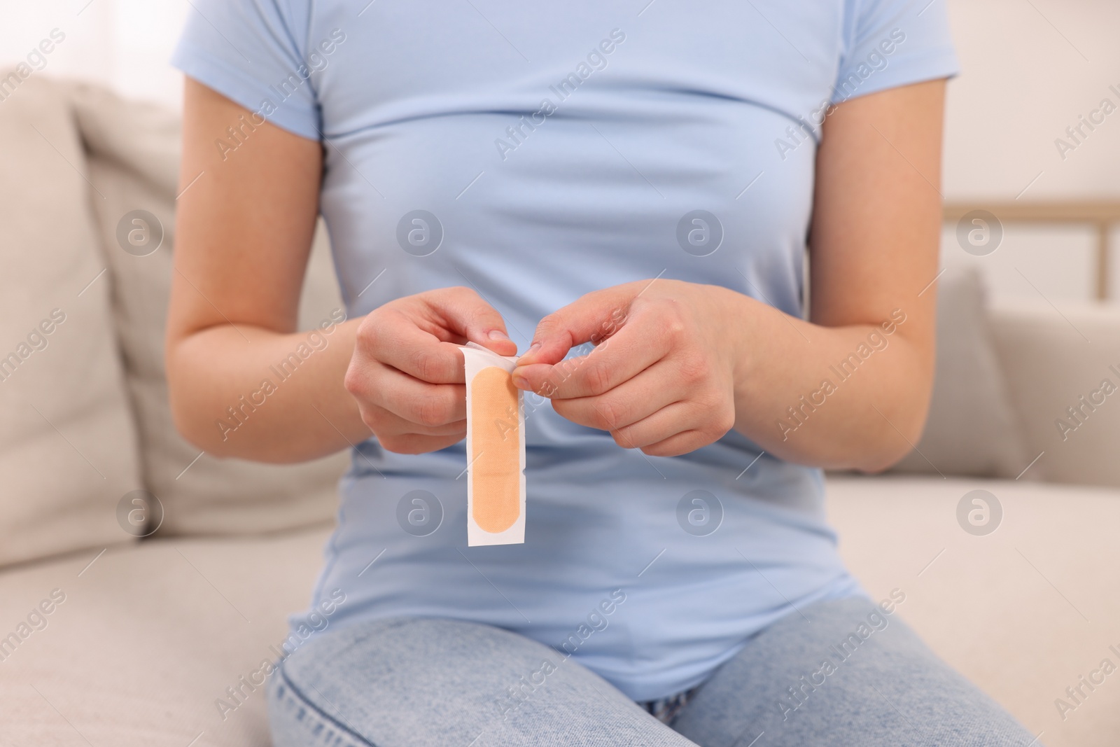 Photo of Woman opening sticking plaster on sofa indoors, closeup