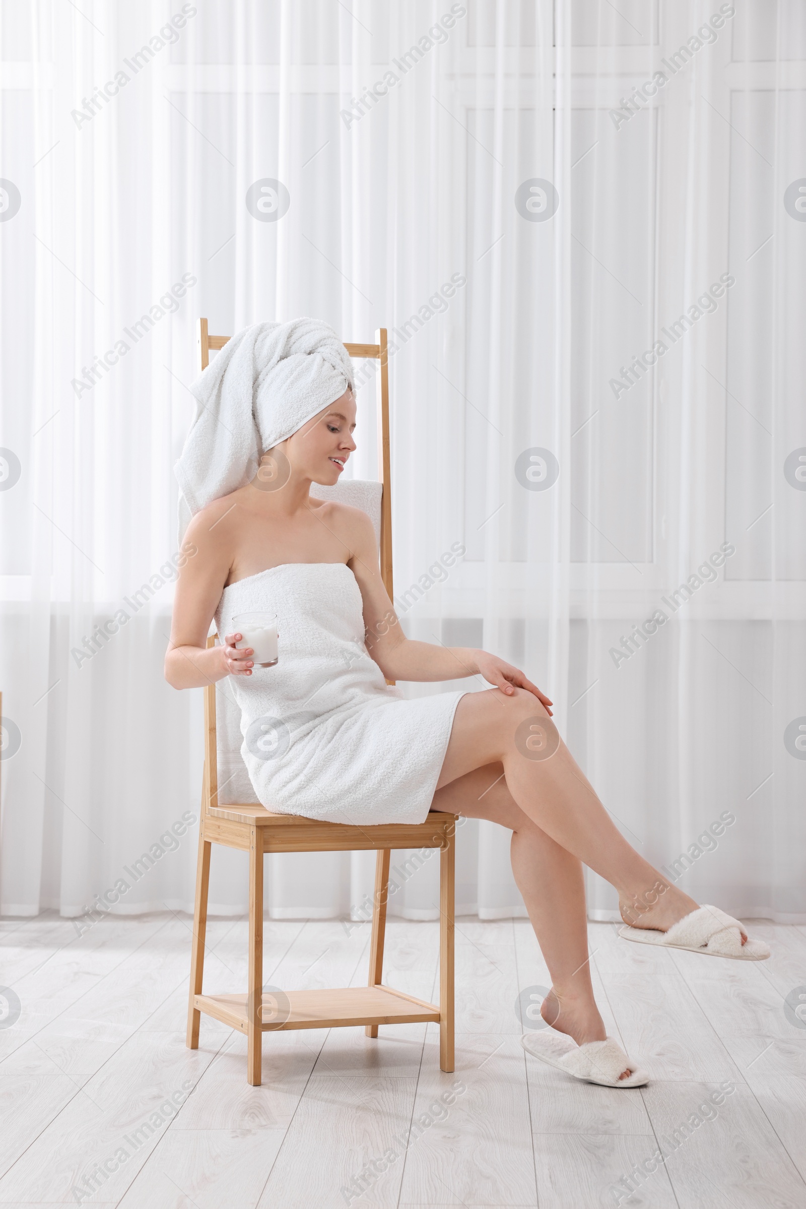Photo of Beautiful young woman applying body cream onto leg indoors