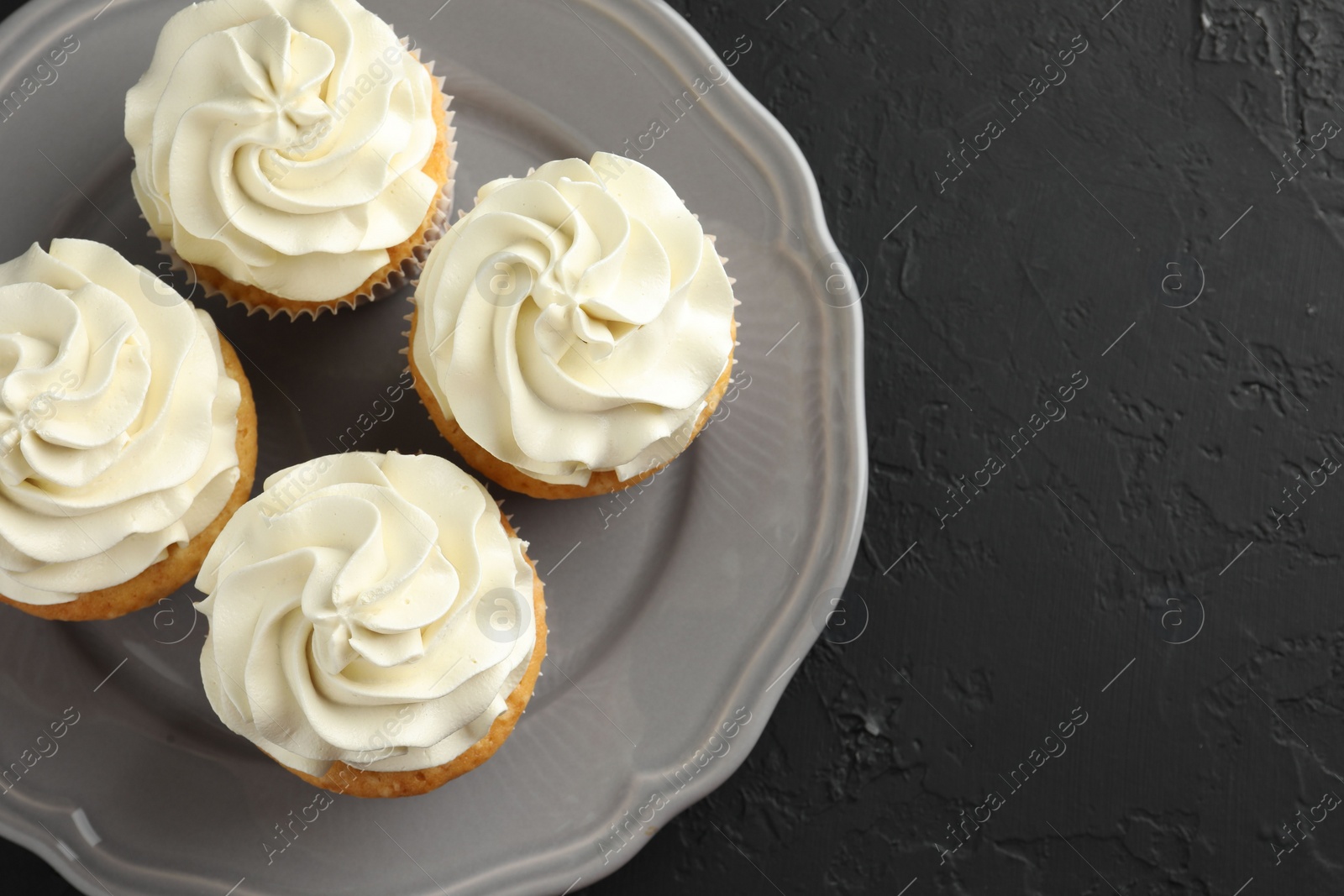 Photo of Tasty cupcakes with vanilla cream on black table, top view. Space for text