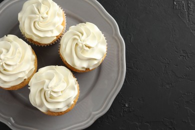 Photo of Tasty cupcakes with vanilla cream on black table, top view. Space for text