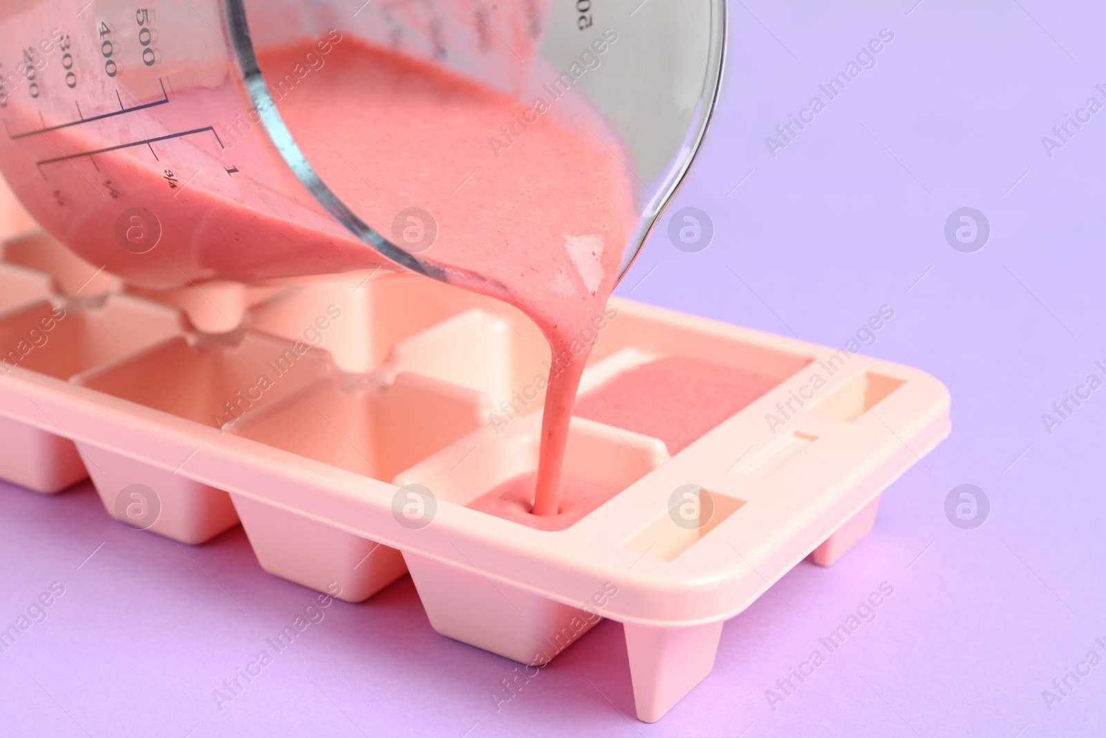 Photo of Pouring smoothie into ice cube tray on table, closeup