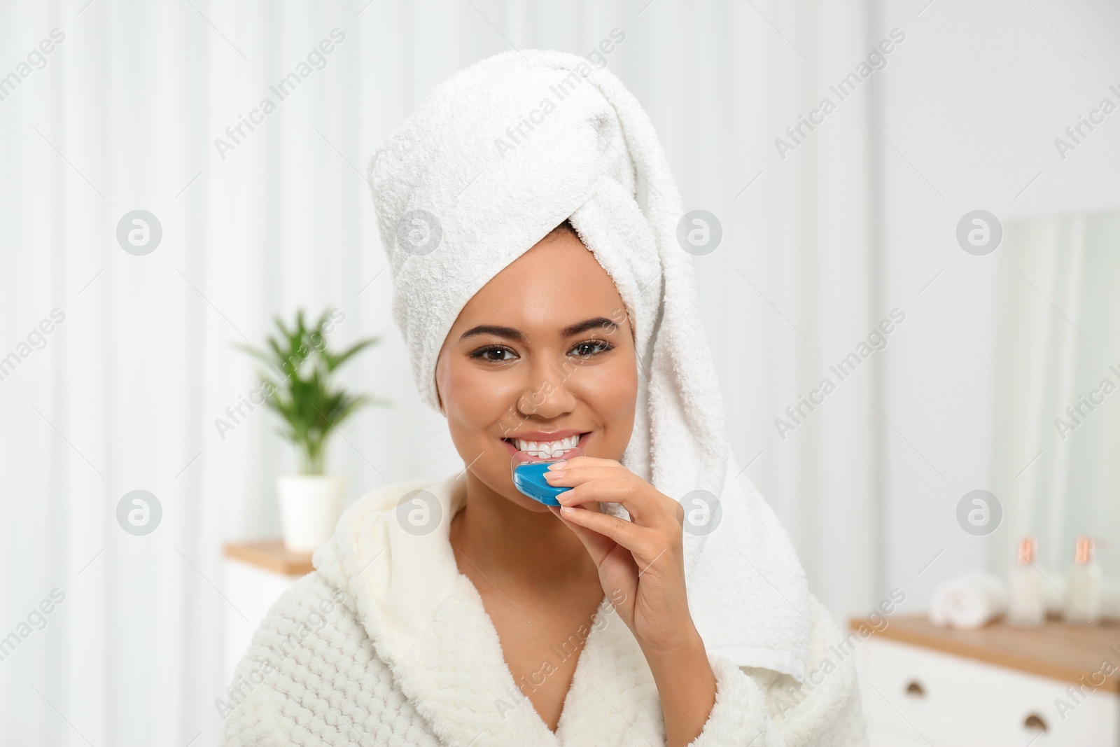 Photo of Young African-American woman using teeth whitening device at home