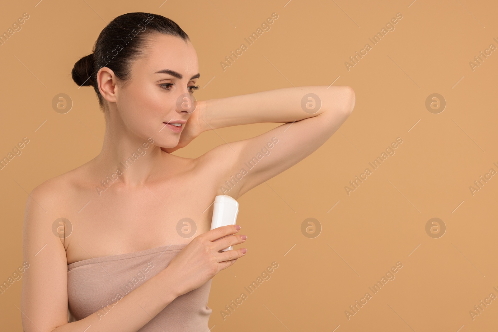 Photo of Beautiful woman applying deodorant on beige background, space for text